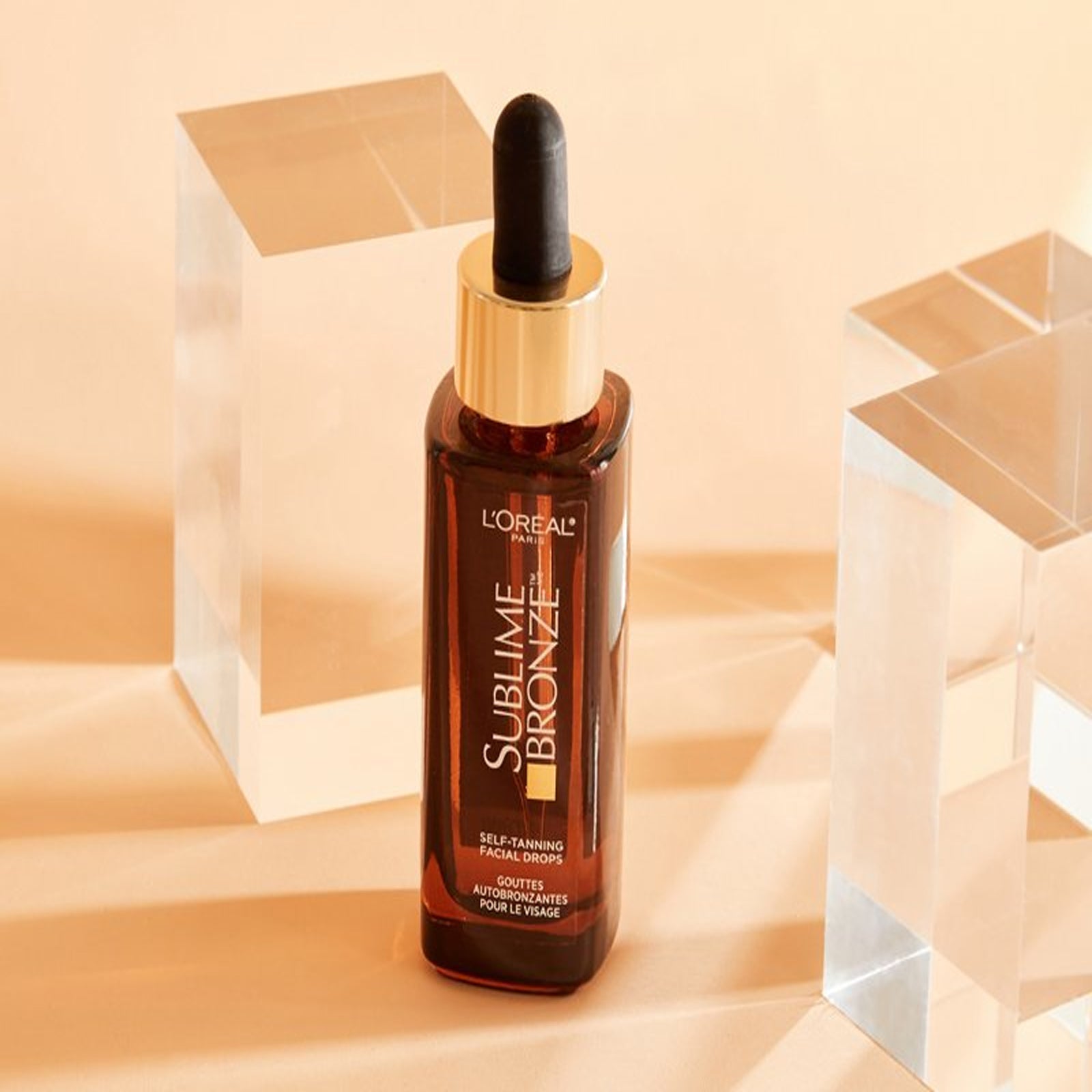 Bottle of L'Oreal Paris Sublime Bronze Self-Tanning Facial Drops, surrounded by hydrating ingredients.
